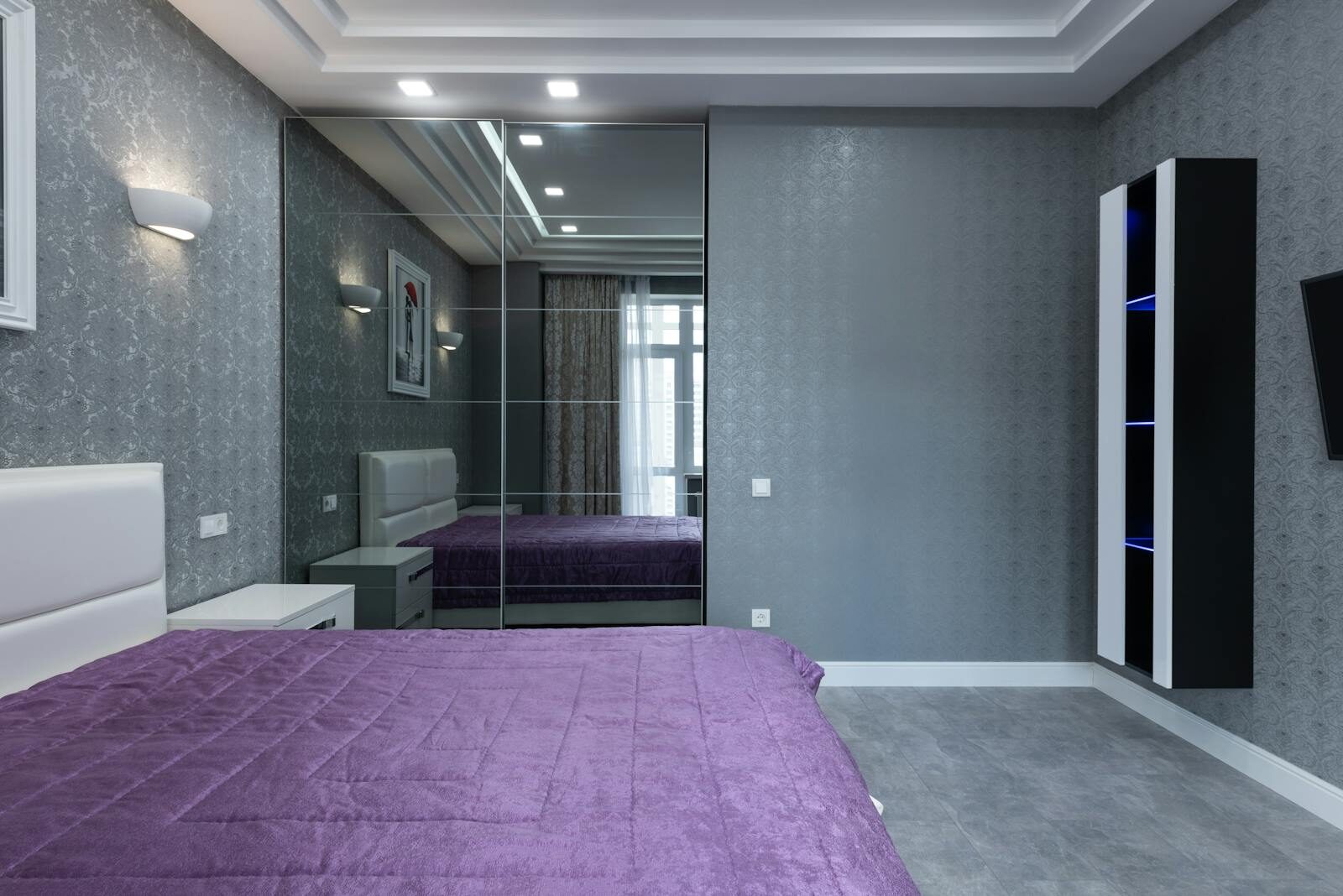 Contemporary bedroom interior with a purple bedspread and mirrored closet, stylish and serene.