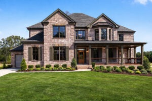 Traditional two-story brick house with a porch, surrounded by a well-maintained green lawn and landscaping, showcasing elegant architectural features.