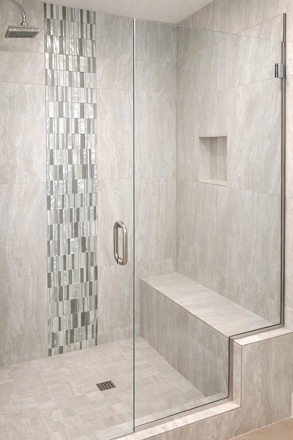 Modern glass shower featuring sleek gray tiles and a built-in bench. A stylish accent wall of glass mosaic tiles adds elegance.