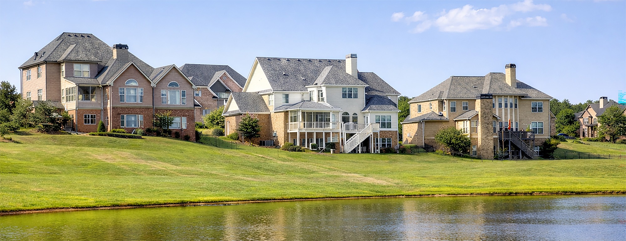Luxurious waterfront homes line a green hillside, reflecting modern architectural designs and serene living by the water.