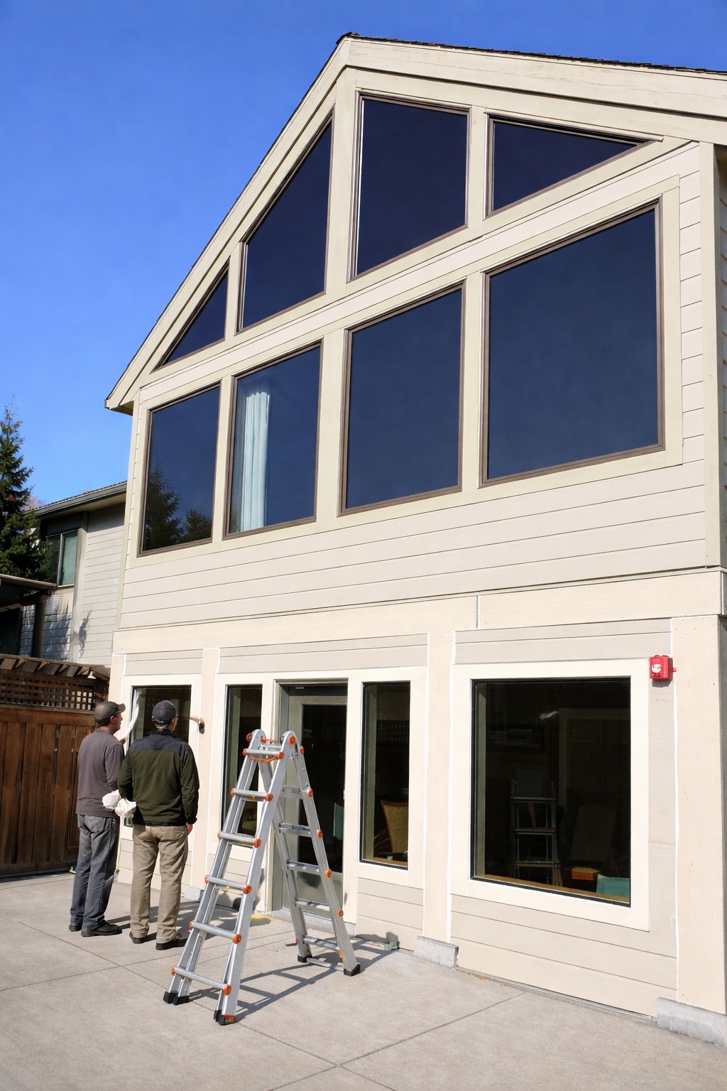 Two men examine a home's exterior, focusing on large, modern windows. A ladder stands nearby, suggesting ongoing maintenance or renovation.