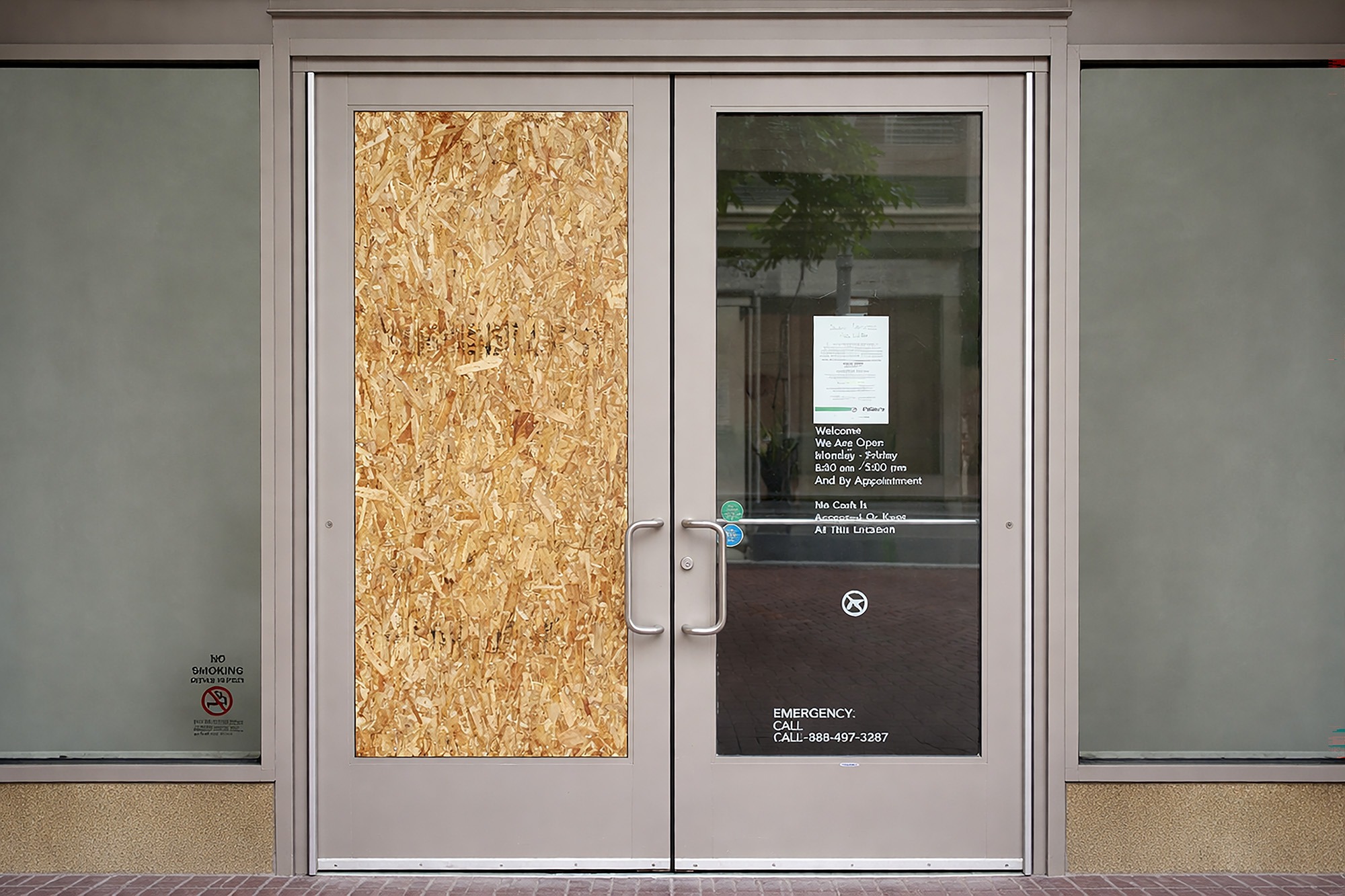 Boarded up entrance with a notice displaying operating hours and contact information, indicating temporary closure.