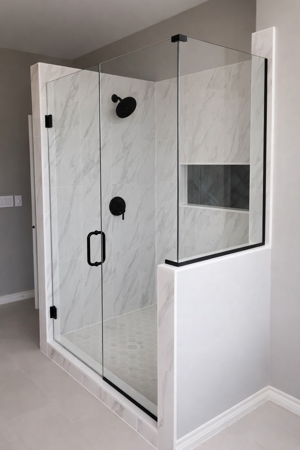 Modern shower design featuring a glass enclosure, white marble tiles, and a black rain showerhead. A clean, minimalist aesthetic enhances the bathroom.